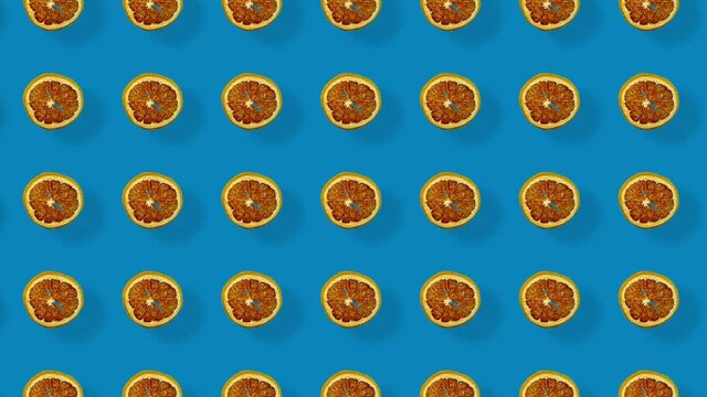 Colorful pattern of dried grapefruit slices on blue background with shadows. Seamless pattern with dried grapefruit chips. Realistic animation. 4K video motion