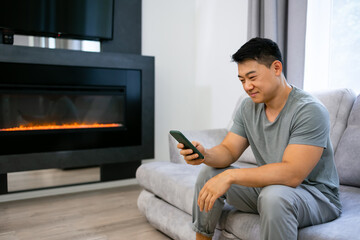 Relaxed man using a smartphone, sitting on the couch in the living room at home, watching the news.