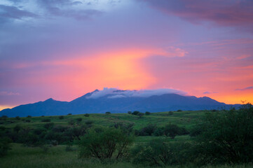 Distant mountain range with foggy top at sunset with green fields.