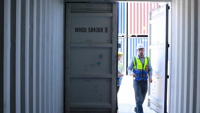 Male engineer foreman and a female worker's assistant wearing helmets use flashlights to inspect empty and dark containers to pack goods for a logistics company import and export business.