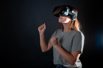 Virtual experience, a young woman using virtual reality glasses, playing a game or interacting with a metaverse, portrait on a black background