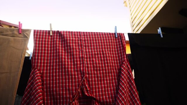 Clean wet clothes are hanging on the rope after laundry and trembling on the wind in a closeup. Fresh shirts and pants are drying in a row on the wash line outdoors at summertime. Chores and housework