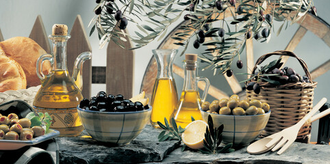 Olive oil and olive berries are on the wooden table under the olive tree. 