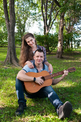 Fototapeta premium Young couple on the grass in the park in the summer, a guy plays the guitar for a girl
