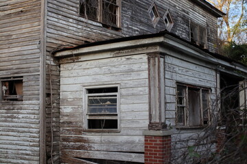 Fototapeta na wymiar Old creepy scary wooden overgrown abandoned mansion corner brick post and window