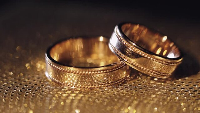Wedding rings lying on shiny golden shining surface with light, close-up macro footage. Rotate spinning clockwise. Pair of marriage symbols. Love of bride and groom, wife and husband. Matrimony symbol