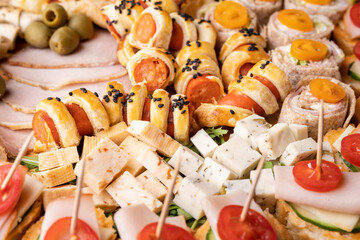 Close up on cheese and ham rolls on the wooden board plate with various food ready to eat - appetizer on the table full frame