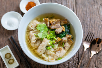 Egg Noodle in Clear Soup, Thailand Street Food, noodle with wonton and crispy pork serving with seasonings on wooden vintage table