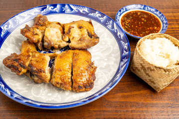A Dish of Grilled Chicken cut in pieces, marinated with garlic, rosemary, thyme and herbs served with sticky rice and special sauce on wooden table