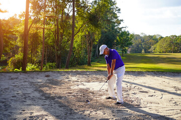 Fototapeta premium The golfer swings her golf club in a shot out of bunker sand.