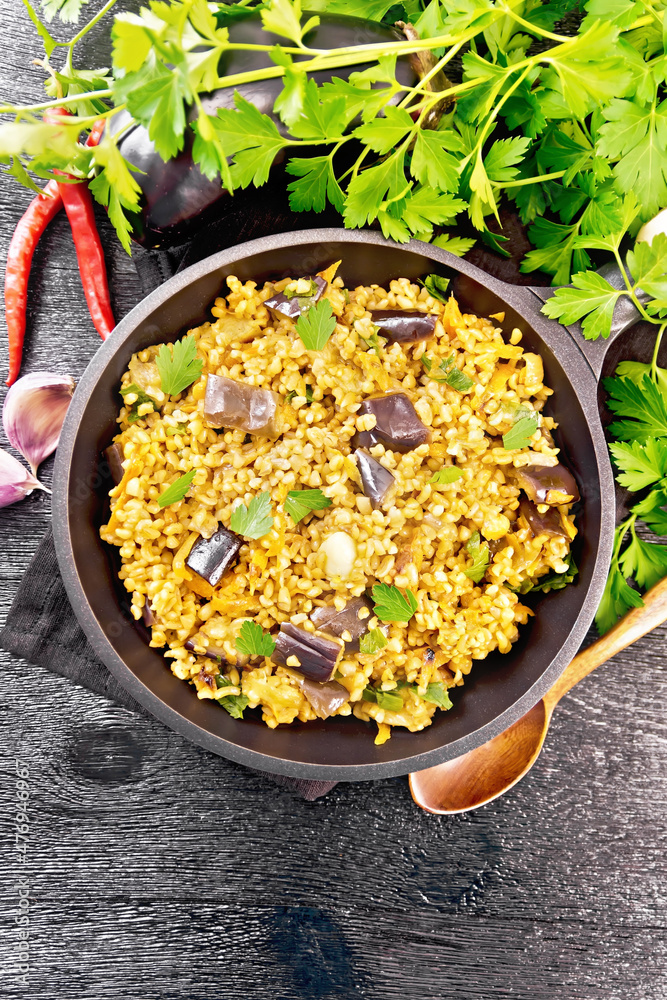 Poster Bulgur with eggplant in pan on dark board top