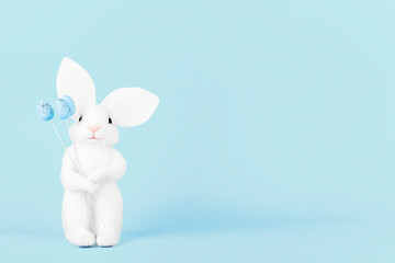 Cute white bunny with Easter eggs on a light blue background, front view. Greeting card for Easter with copy space.