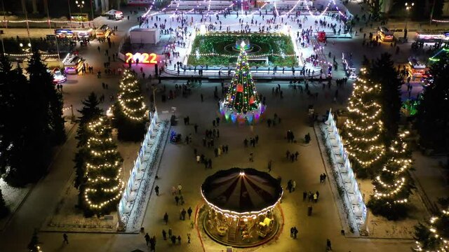 Christmas tree on the city square, aerial view. Fabulous Christmas glowing illumination, green tree in the city center. Christmas Market, aerial view. Christmas carousels, and ice rink