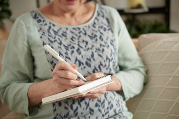 Cropped image of senior woman writing in diary or gratitude journal