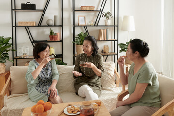 Group of senior female friends meeting at home to drink tea with cookies and discuss news