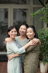 Portrait of hugging senior female friends standing at house front door