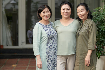 Group of cheerful elderly female friends standing at house entrance