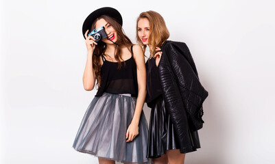 fashion portrait of two elegant stylish  women wearing a leather  skirt and black hat , holding  retro camera.  Posing against white background.