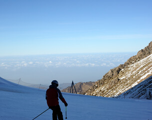 Active lifestyle and sports: rest in a ski resort. Skiing, snowboarding. Nice alpine view. Skiers and skateboarders are driving fast against the blue sky, above the clouds