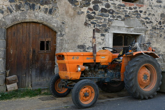 Vieux tracteur orange devant une ancienne grange dans un petit village du Puy de dome