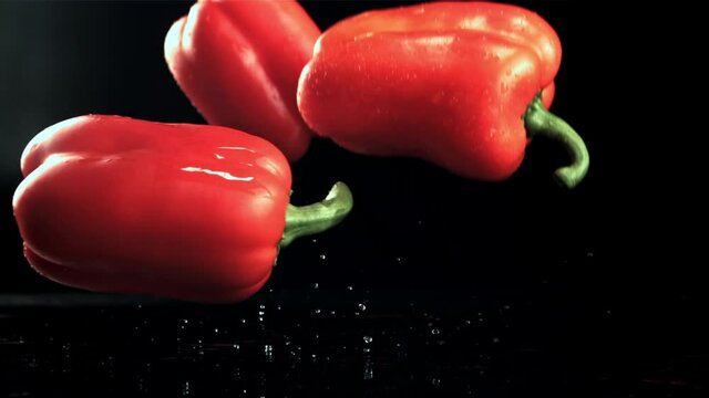 Red sweet peppers fall on the table. On a black background.Filmed is slow motion 1000 frames per second. High quality FullHD footage