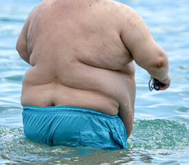 A fat man is swimming in the sea.