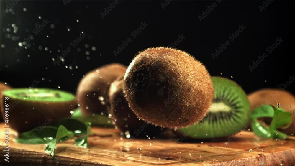 Poster a ripe kiwi falls on a cutting board with splashes of water. on a black background. filmed is slow m