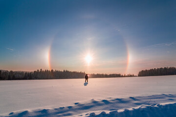 silhouette of a man standing in a snowy field and looking at the sun halo