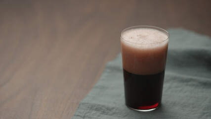 pour dark berry drink in tumbler glass on walnut table with copy space