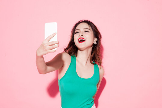 Portrait Of A Happy Asian Lady Holding Mobile Phone And Dancing Isolated Over Pink Background