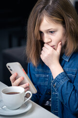 A teenager girl looks surprised at the smartphone screen.