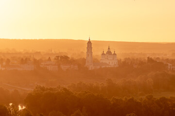 Naklejka premium Russian Orthodox Church in the morning fog at dawn in the middle of the forest lit by golden light