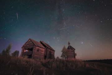 Old abandoned wooden chapel and building unde night sky full of stars and meteors of Perseids