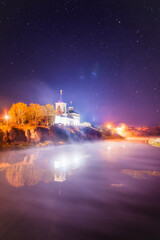 The Russian Orthodox Church stands on a rock by the river, shrouded in fog, under a beautiful night sky