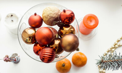Christmas toys of red and bronze color, lie in a glass plate, candles red and white, tangerines photo in the afternoon