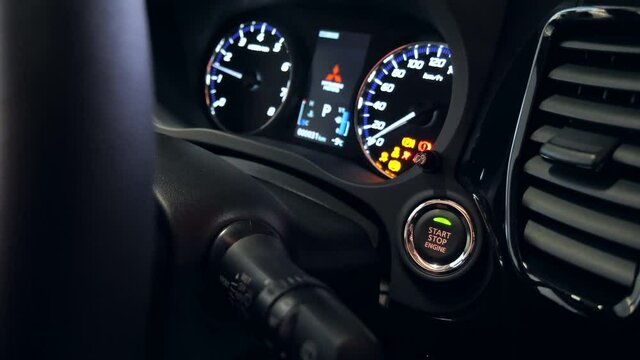 A woman's finger presses the car start button. She starts the engine. Shooting close-up