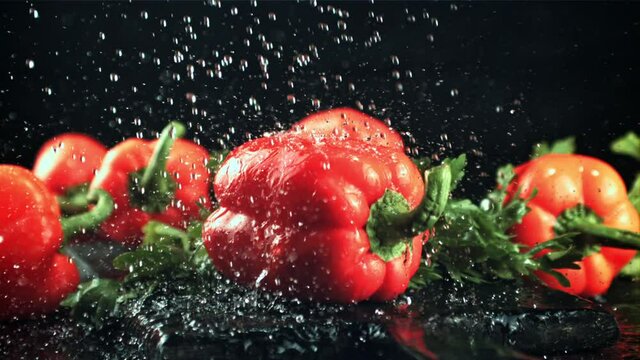 Drops of water with splashes fall on the sweet pepper. On a black background. Filmed is slow motion 1000 fps.