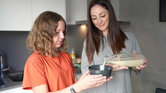A woman puts rice and oatmeal drink into her teenage daughter's glass. Mother and daughter preparing healthy breakfast of fruits and oatmeal flakes and alternative drink to milk.