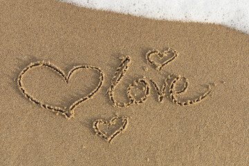 Hearts drawn on the sand with the inscription love with the sea wave.