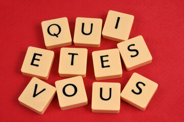 Qui êtes-vous écrit en français avec des lettres de l'alphabet en gros plan sur fond rouge - obrazy, fototapety, plakaty