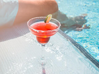 Beautiful glass with a refresh cocktail and an attractive man on the background of the swim pool. Top view, close-up. Vacation and travel concept. Moments of celebration