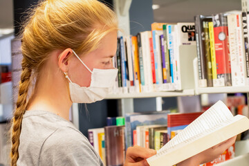 Teenage girl wearing face mask with the book in her hands at the library during the COVID-19 pandemic