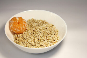 Oatmeal with whole tangerine. In a white plate.