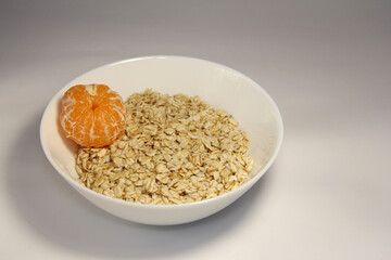 Oatmeal with whole tangerine. In a white plate.
