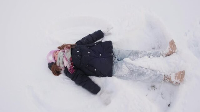 Little happy girl lies in the snow and makes a snow angel. Christmas, vacation, vacation