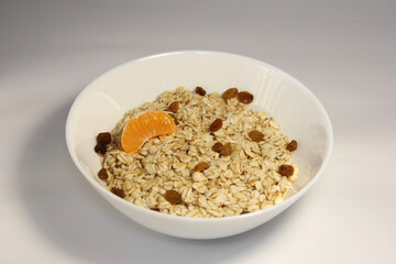 Oatmeal with tangerine slices and raisins. In a white bowl.