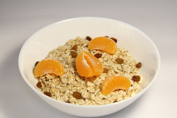 Oatmeal with tangerine slices and raisins. In a white bowl.