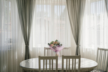 white oval table with a bouquet of flowers in a room with large windows. 