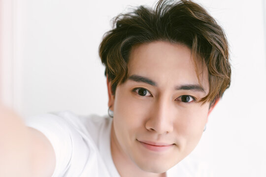 Closeup of beautiful young Asian man in casual clothes taking selfie looking at the camera on isolated over white background. Natural Beauty, Healthy man.