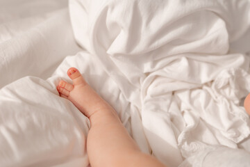 closeup of the bare feet of a baby in a white bodysuit lying on a white bed. High quality photo